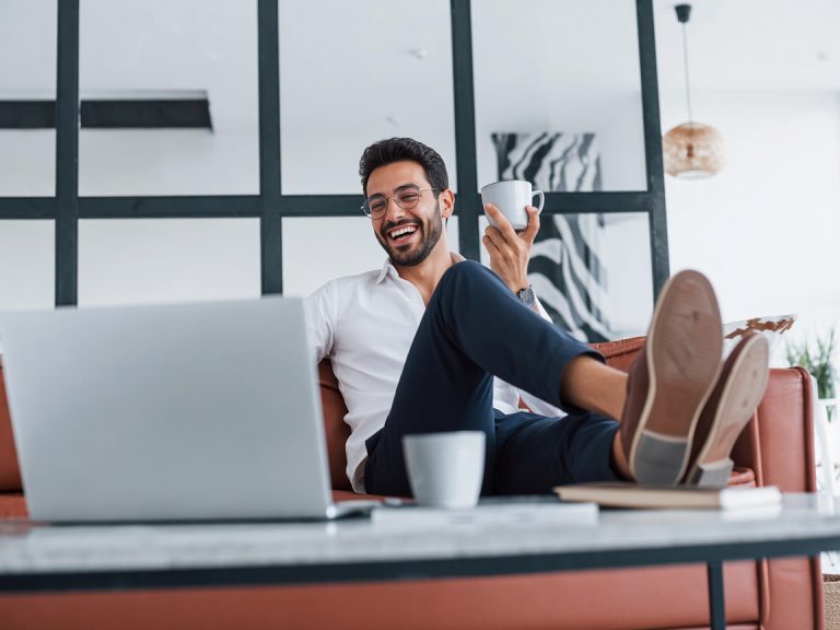 With laptop. Caucasian young guy in elegant white shirt indoors at home