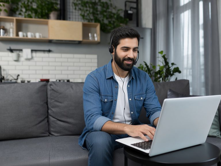 Person comfortably attending a mental health awareness session online while seated on a sofa with a computer and headset.